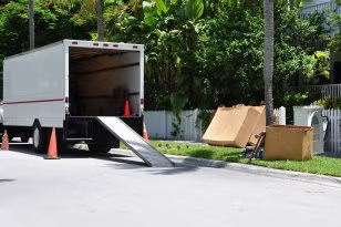 White moving truck with ramp parked roadside beside cardboard boxes and cones.