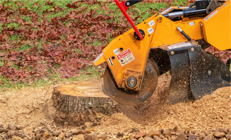 A stump grinder is cutting a tree stump in a yard.