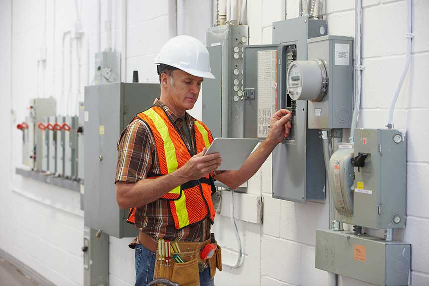 Electrician Repairing Fuse Box and Holding Digital Tablet — Richmond, VA — Beckstoffer Welsh Inc. Electrician Repairing Fuse Box and Holding Digital Tablet — Richmond, VA — Beckstoffer Welsh Inc.