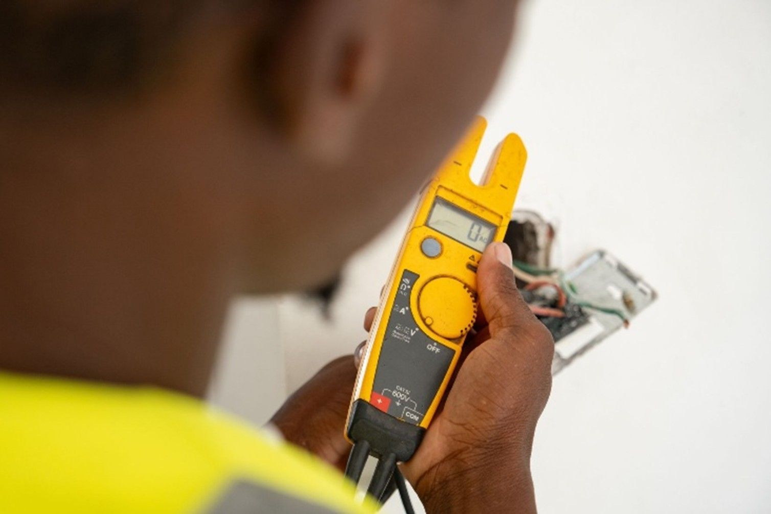 An electrician using a voltage tester to check wiring inside an open wall socket during repair