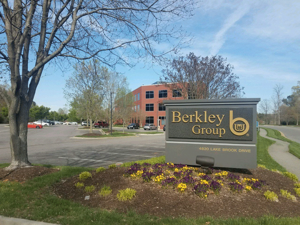 Sign for Berkley Group outside an office building and a parking area with flowers and trees.