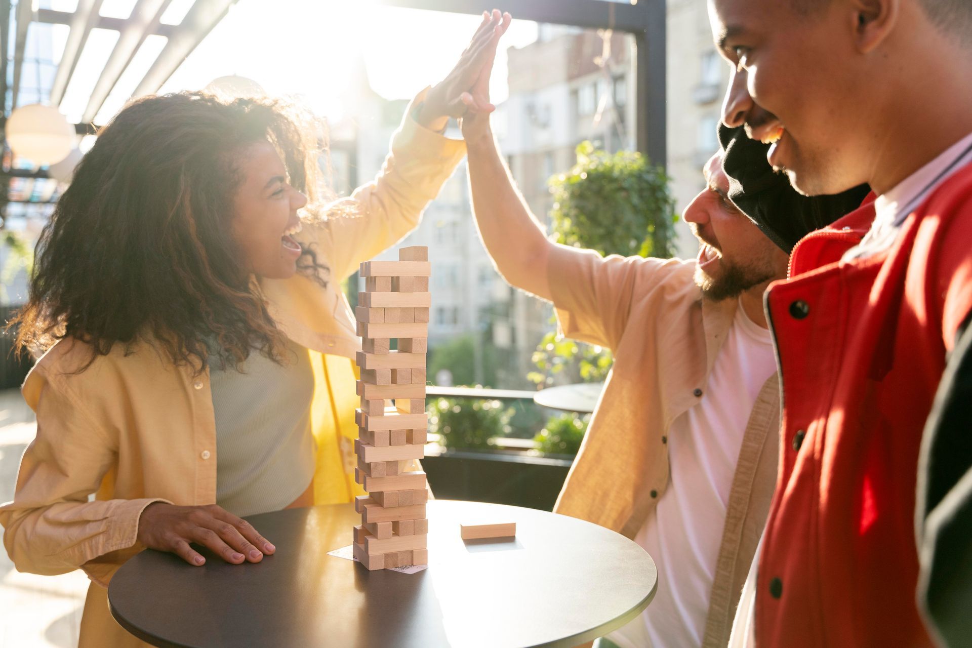 Des personnes jouent au Jenga et se tapent dans la main, sur une terrasse ensoleillée.