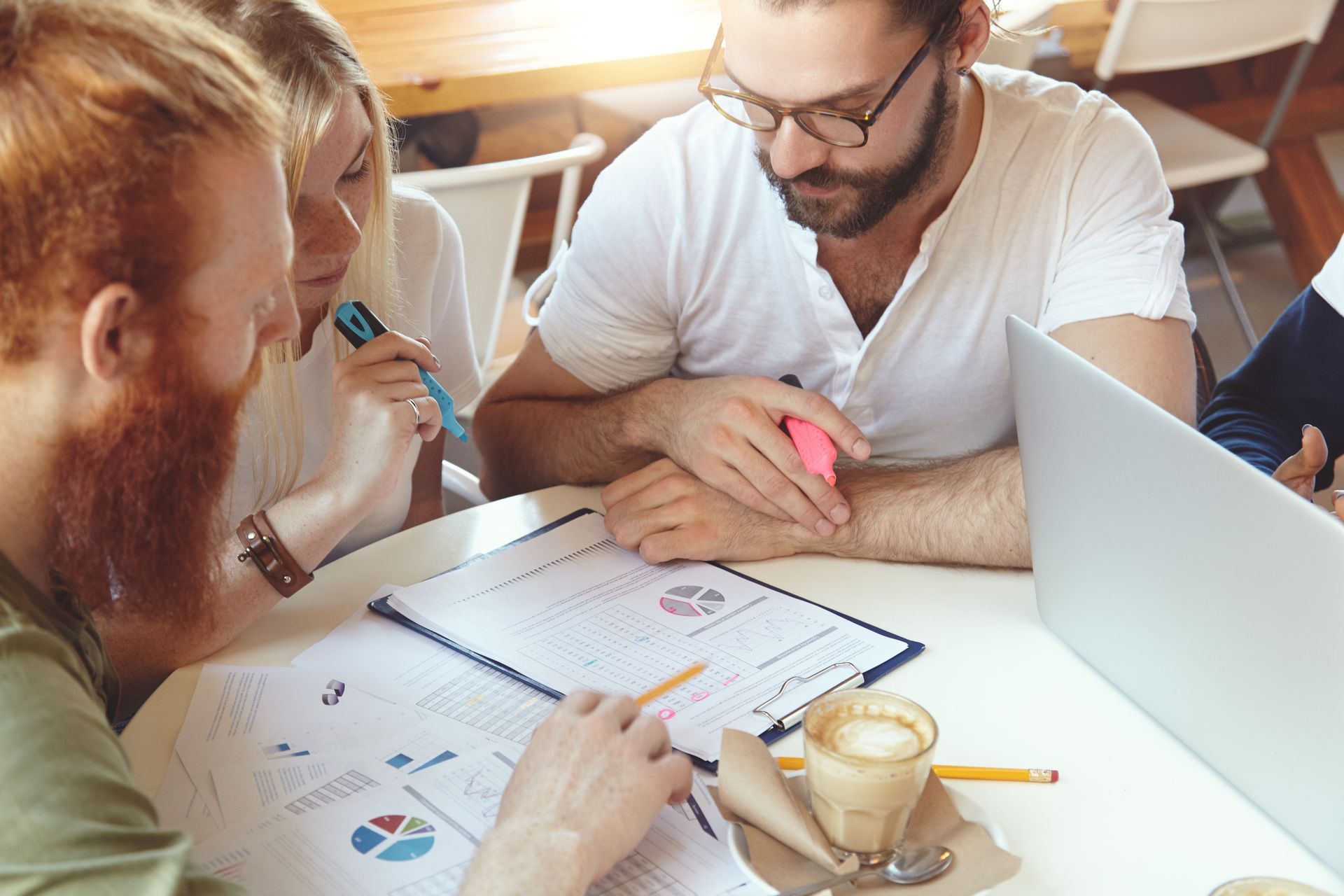 Des personnes qui collaborent autour d'une table avec des graphiques, un ordinateur portable et du café.