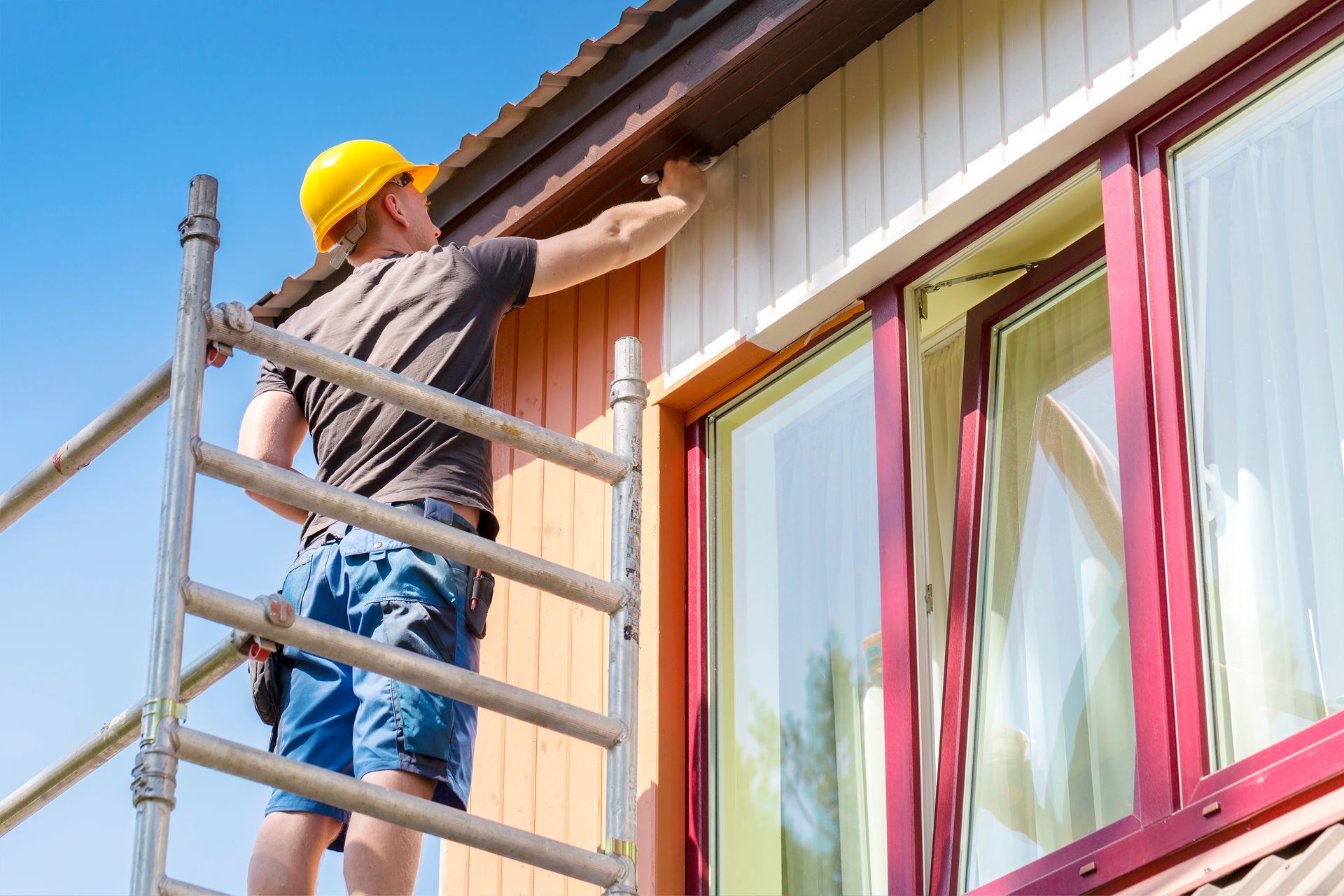 Painter on a ladder painting the trim of a house; sunny day.