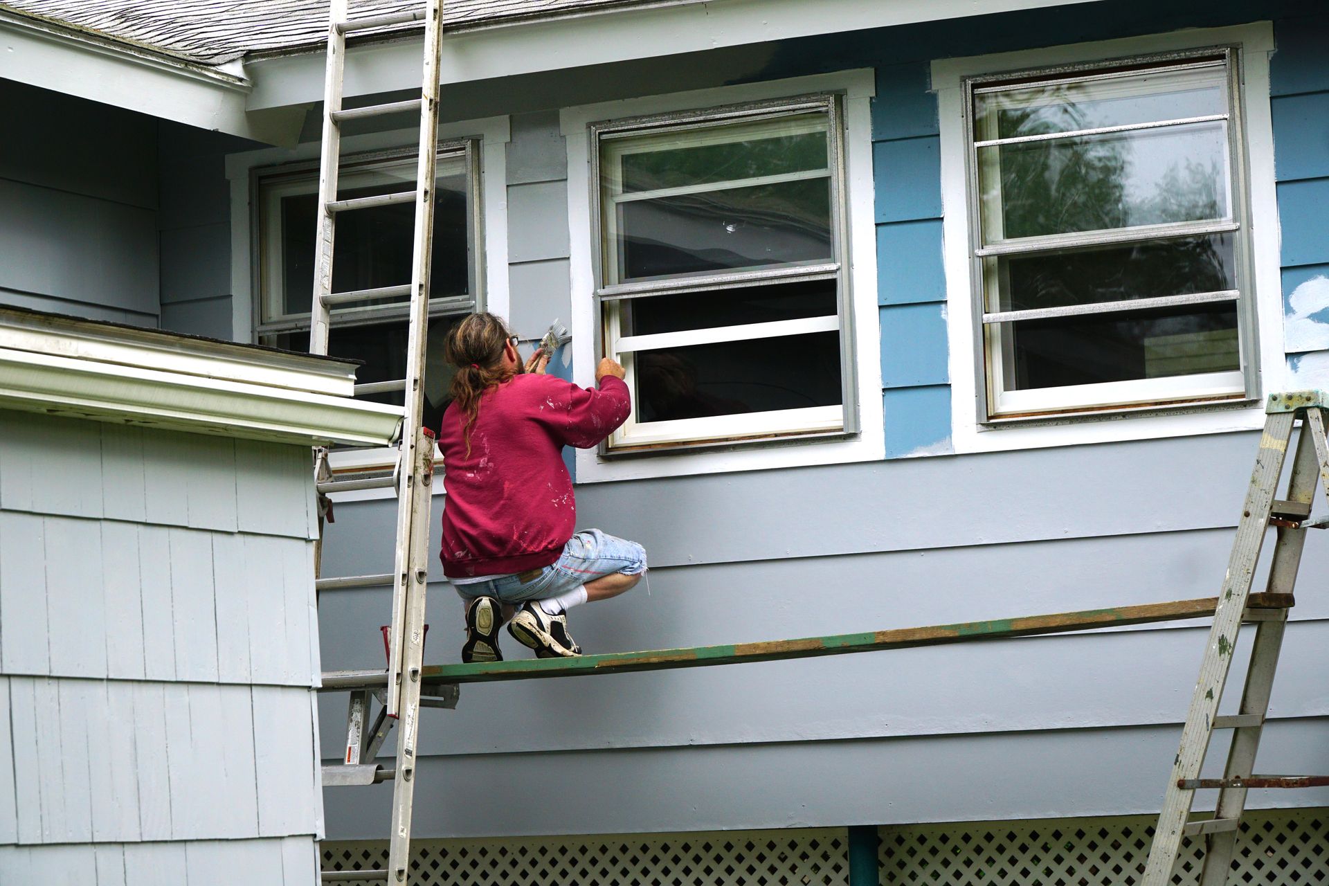 Person on scaffolding, cleaning windows of a blue house.
