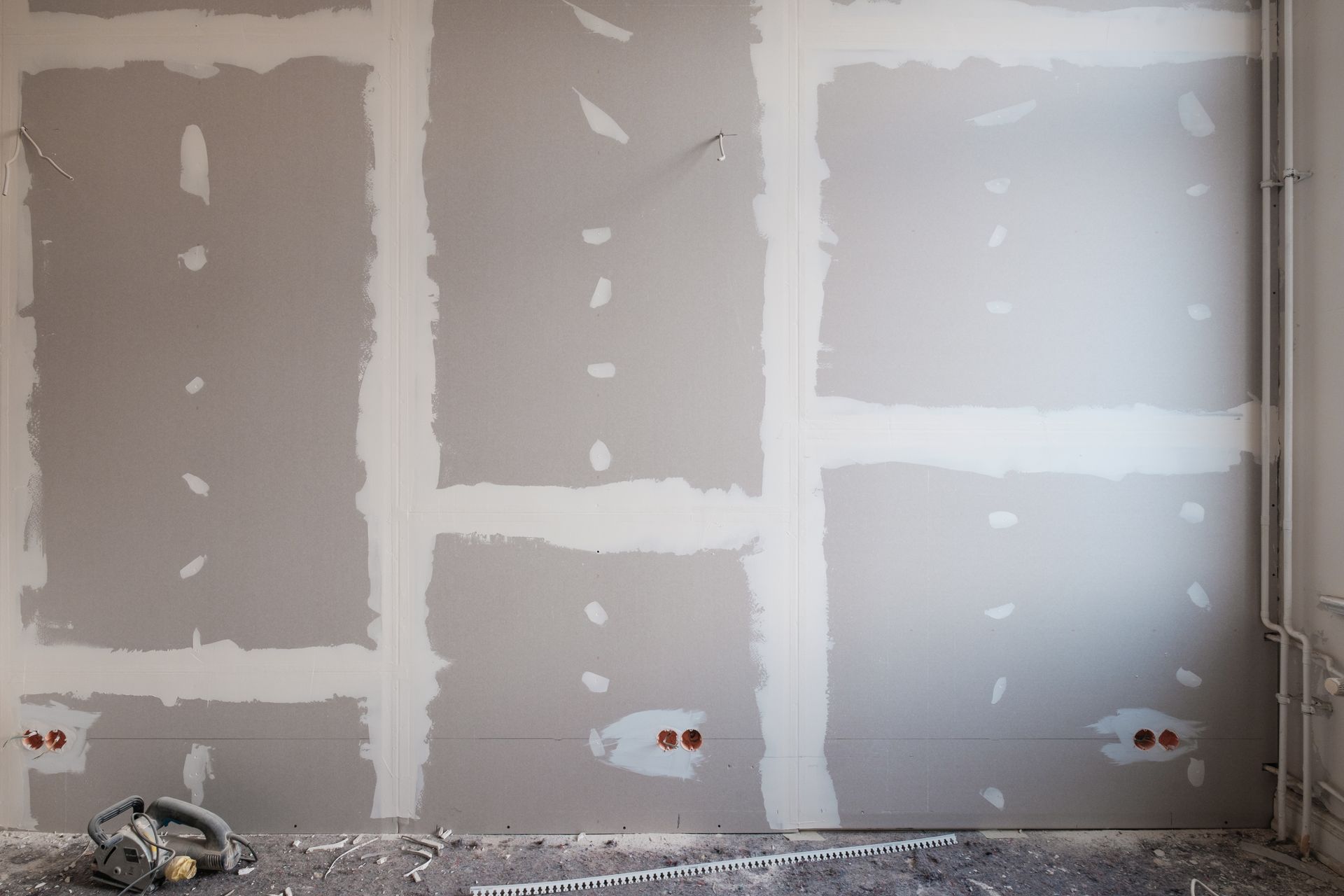 Wall with drywall partially finished, showing taped seams and filled screw holes.