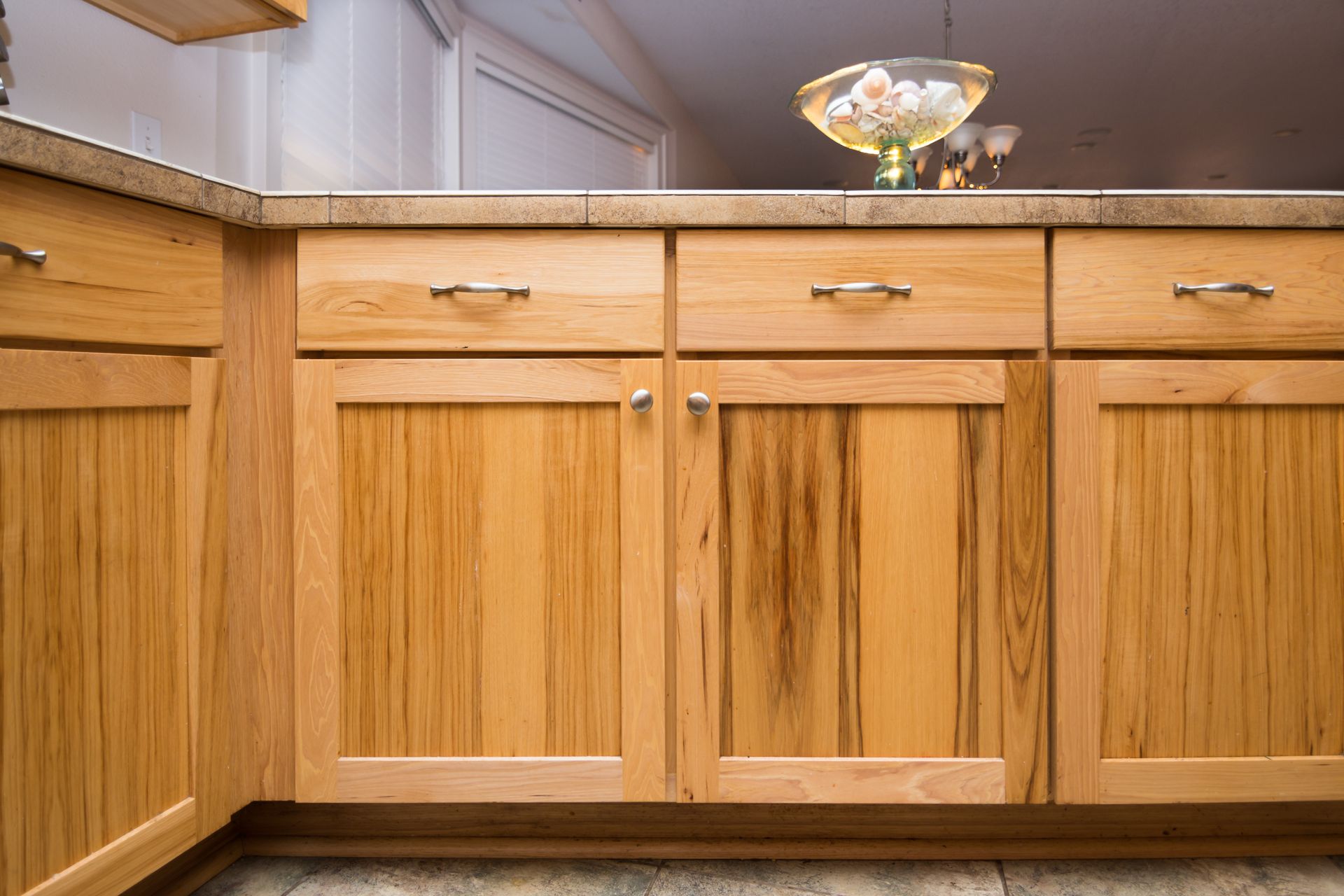 Light wood kitchen cabinets with silver handles under a granite countertop.