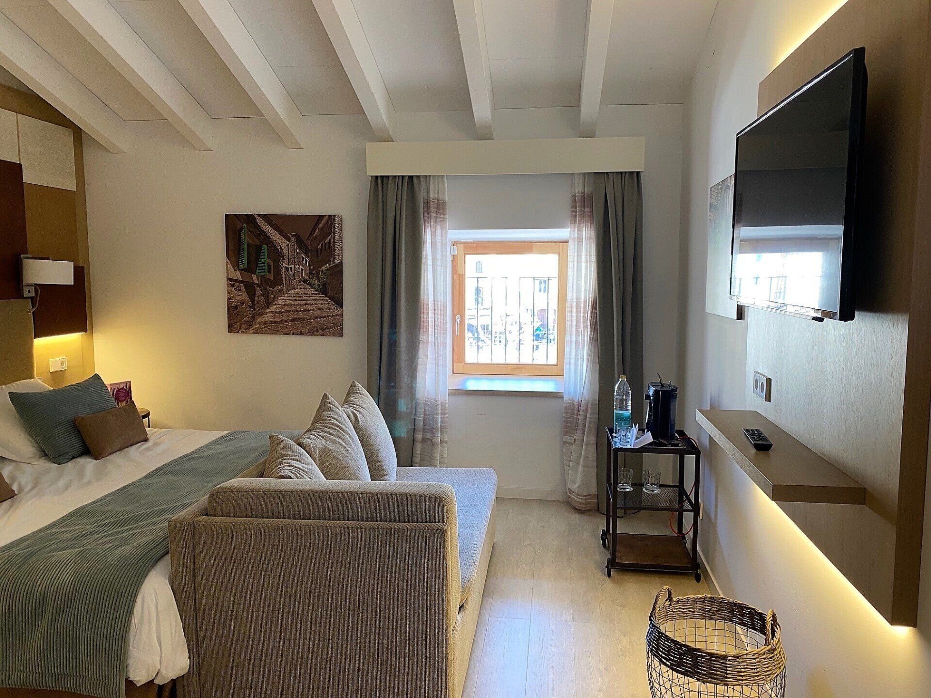 Hotel room with a bed, sofa, window, and a wall-mounted TV.