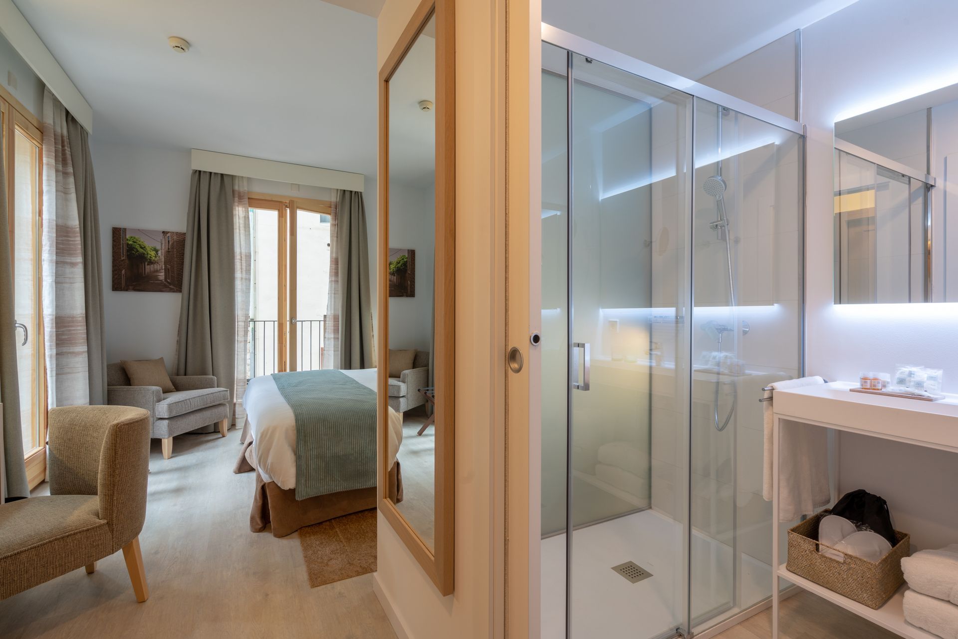 Bedroom and bathroom suite with neutral tones, featuring a shower, bed, and seating area.