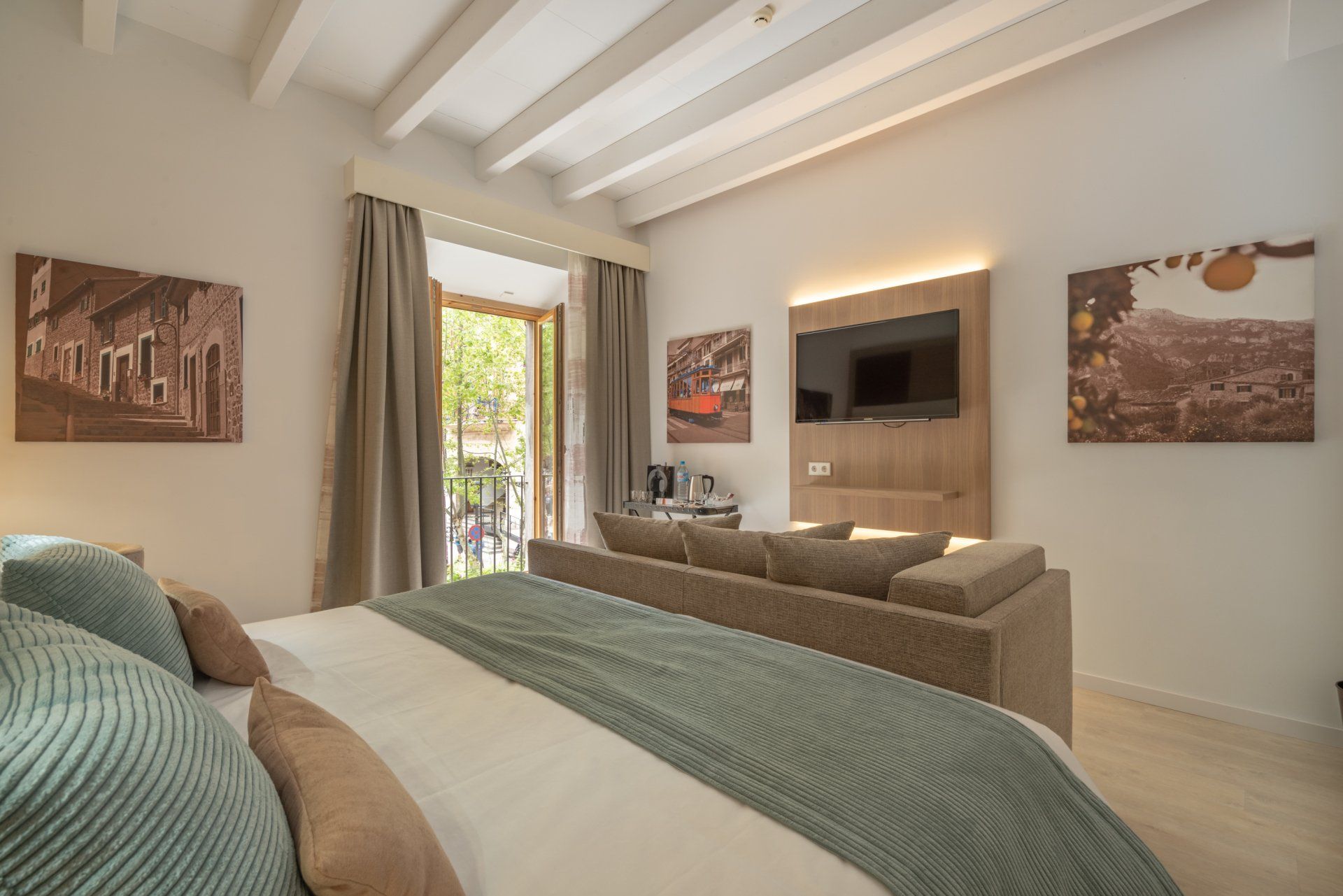 Spacious hotel room with king bed, sofa, balcony, and art.