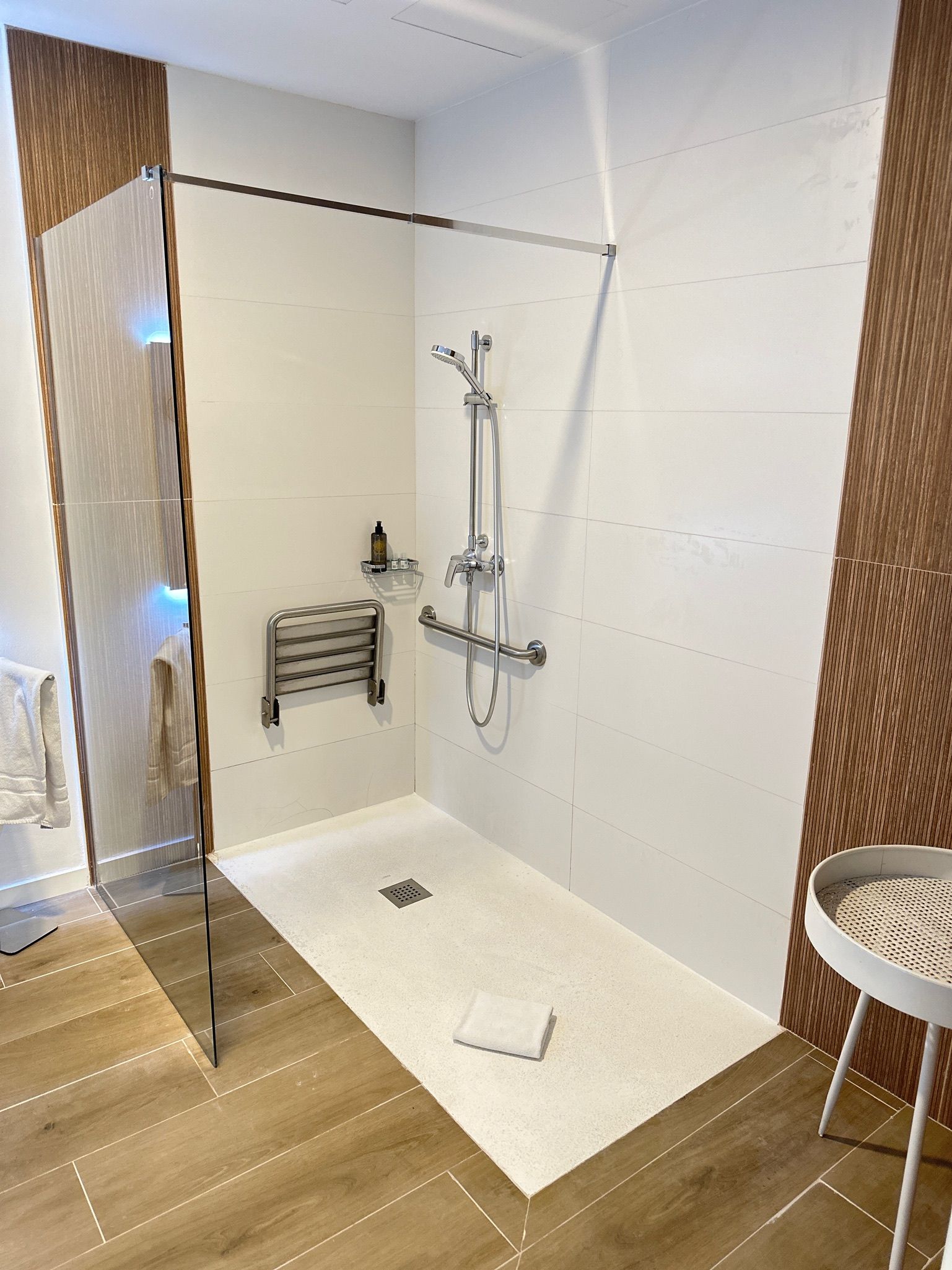 Accessible shower with grab bars, shower seat, and glass enclosure, white and brown tile.