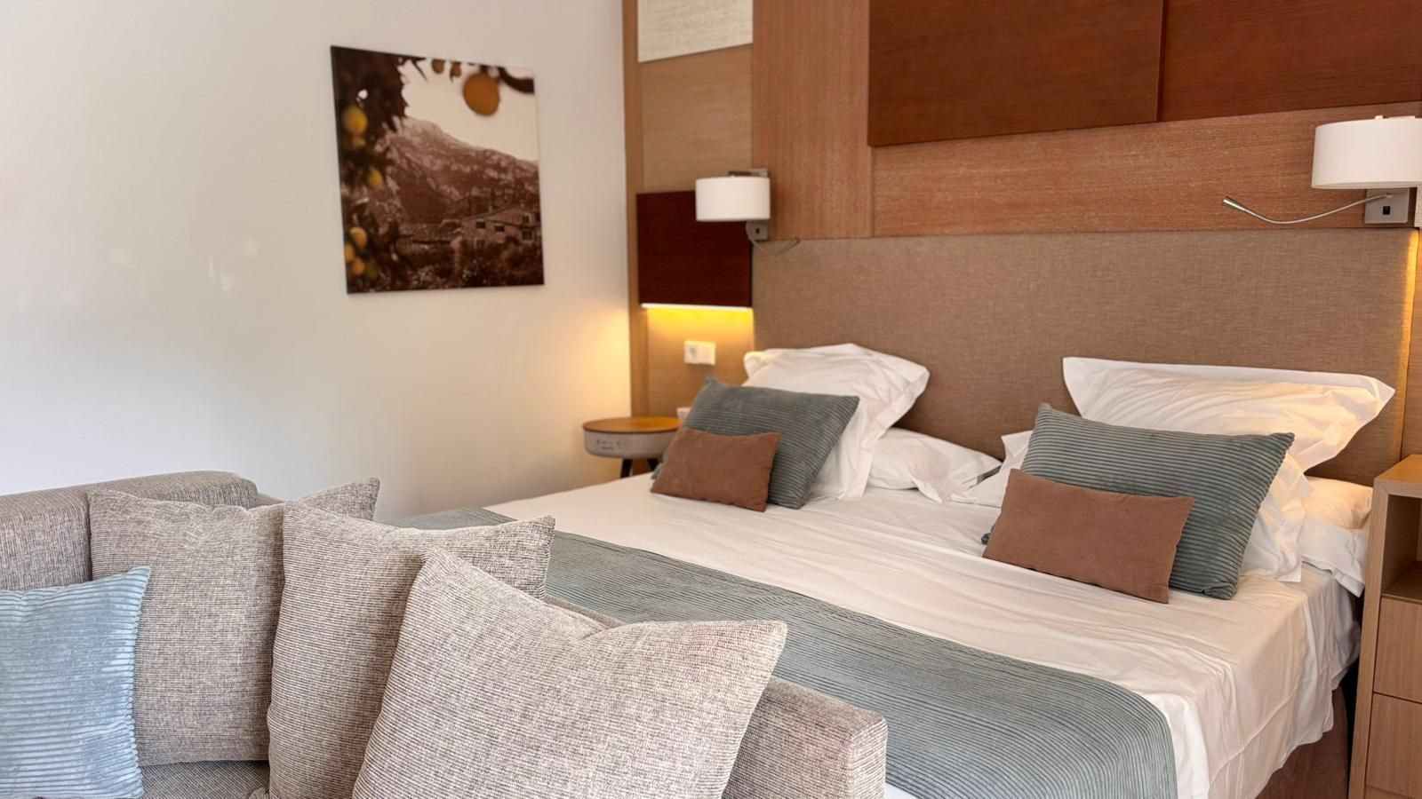 Hotel bedroom with a large bed, sofa, nightstand, and wall art.
