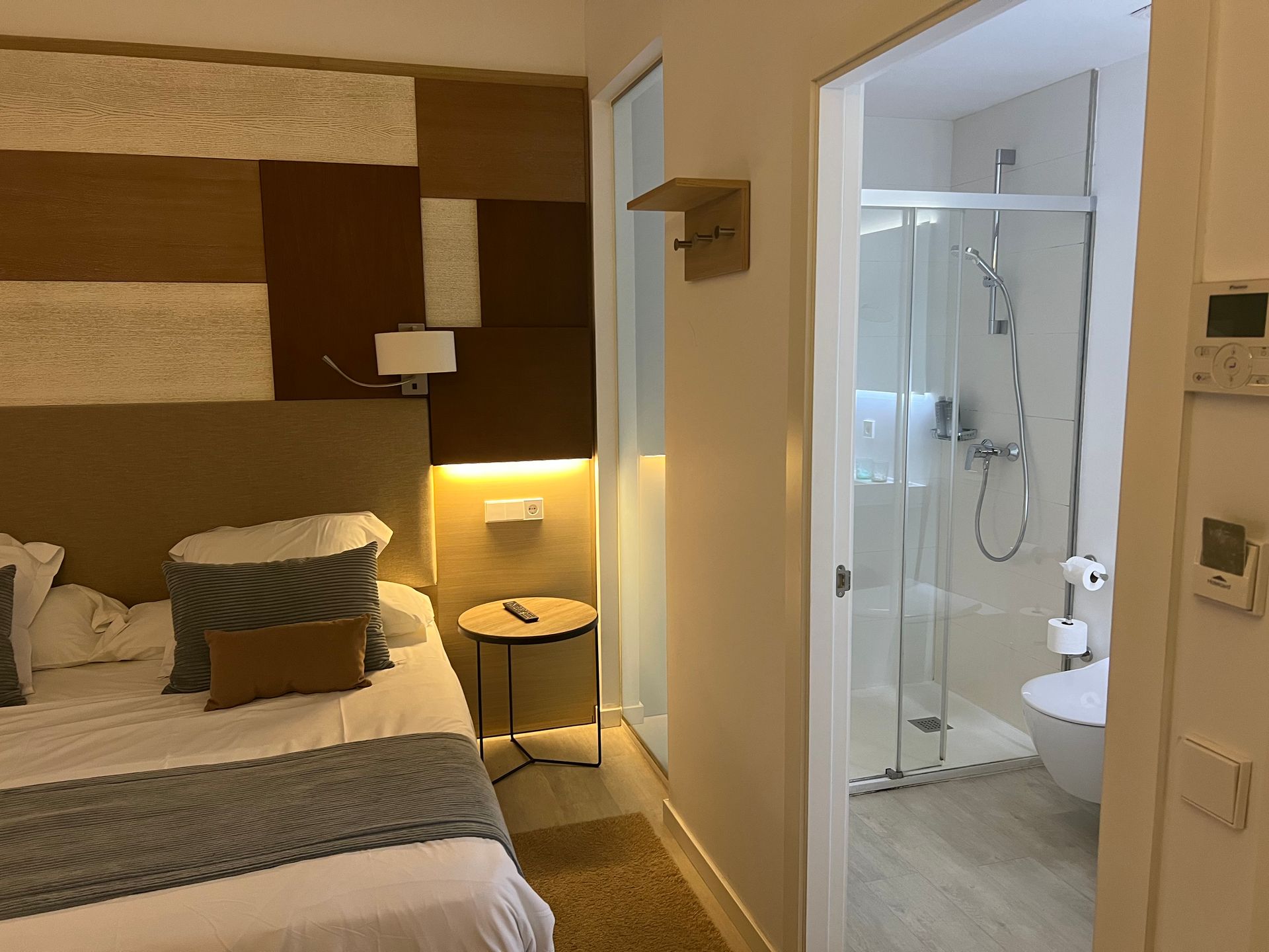 Bedroom with a bed, small table, and bathroom entrance. Light wood and neutral colors dominate.