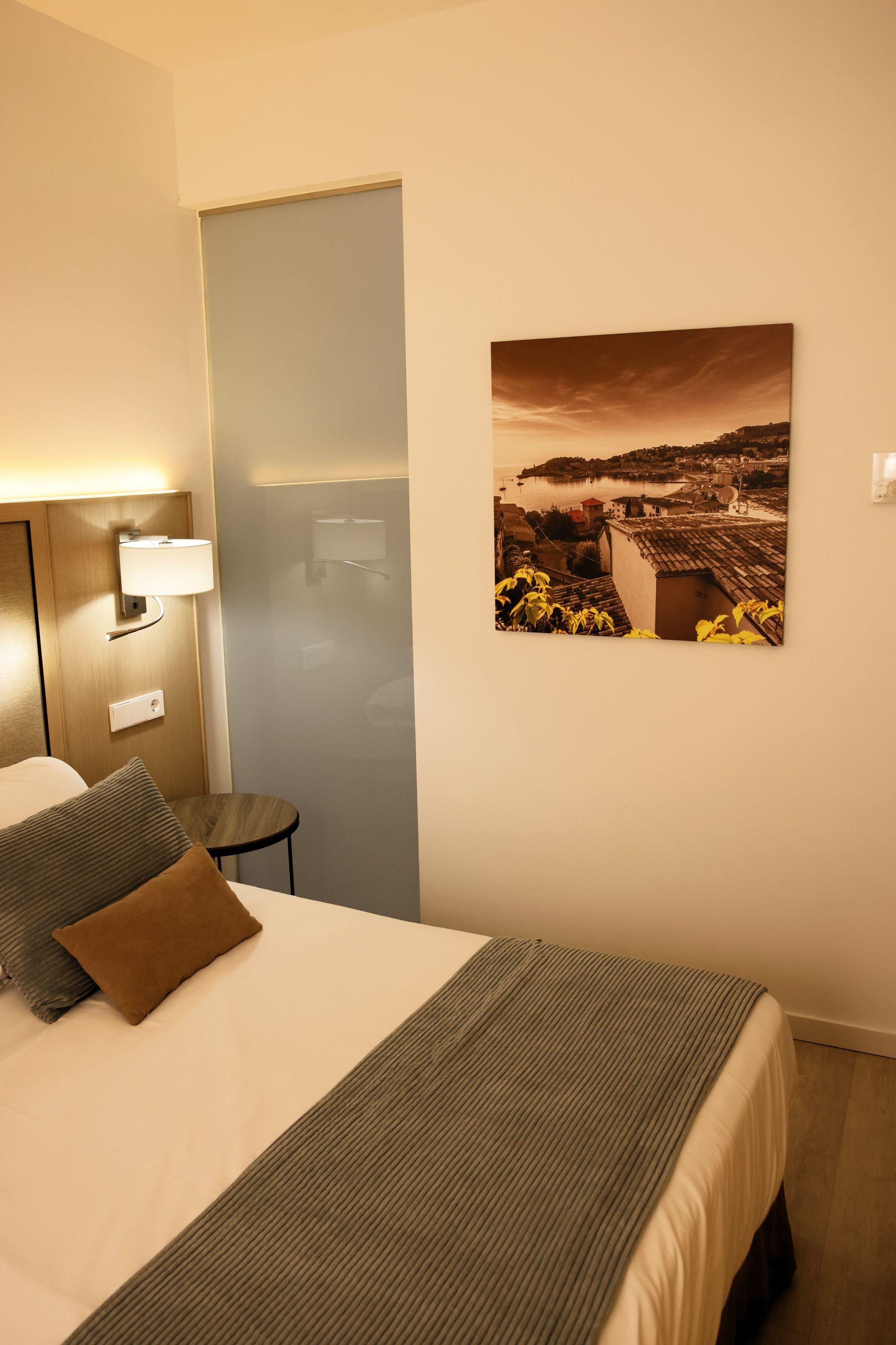 Cozy hotel room with a single bed, art on the wall, and a blue-gray throw blanket.