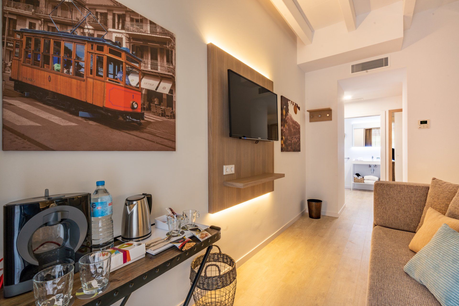 Hotel room interior with TV, sofa, and desk with coffee machine. Artwork of a tram.