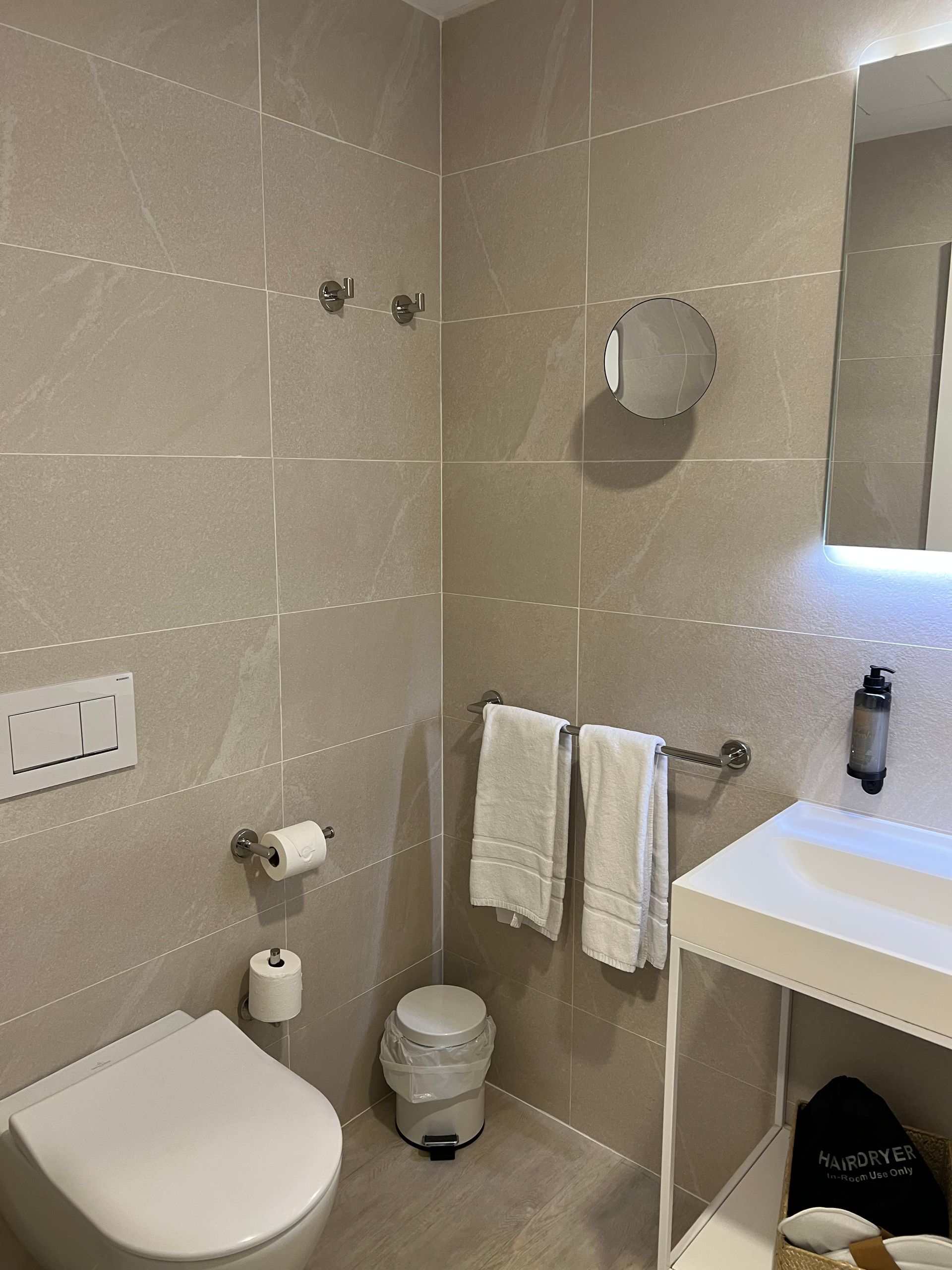 Small bathroom with toilet, sink, and towel rack on a light gray tiled wall.