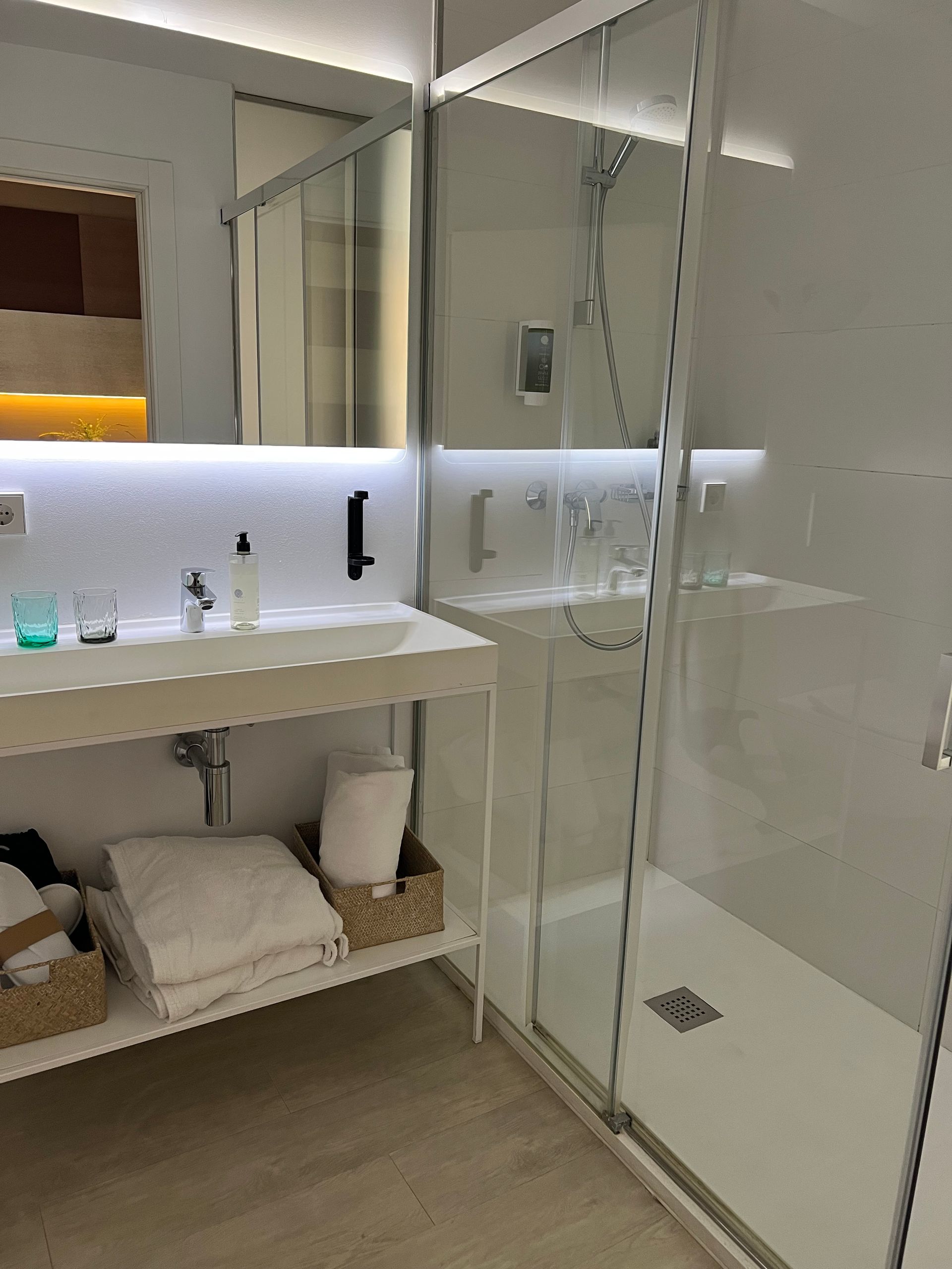 Modern white bathroom with glass shower, floating sink, and towels.
