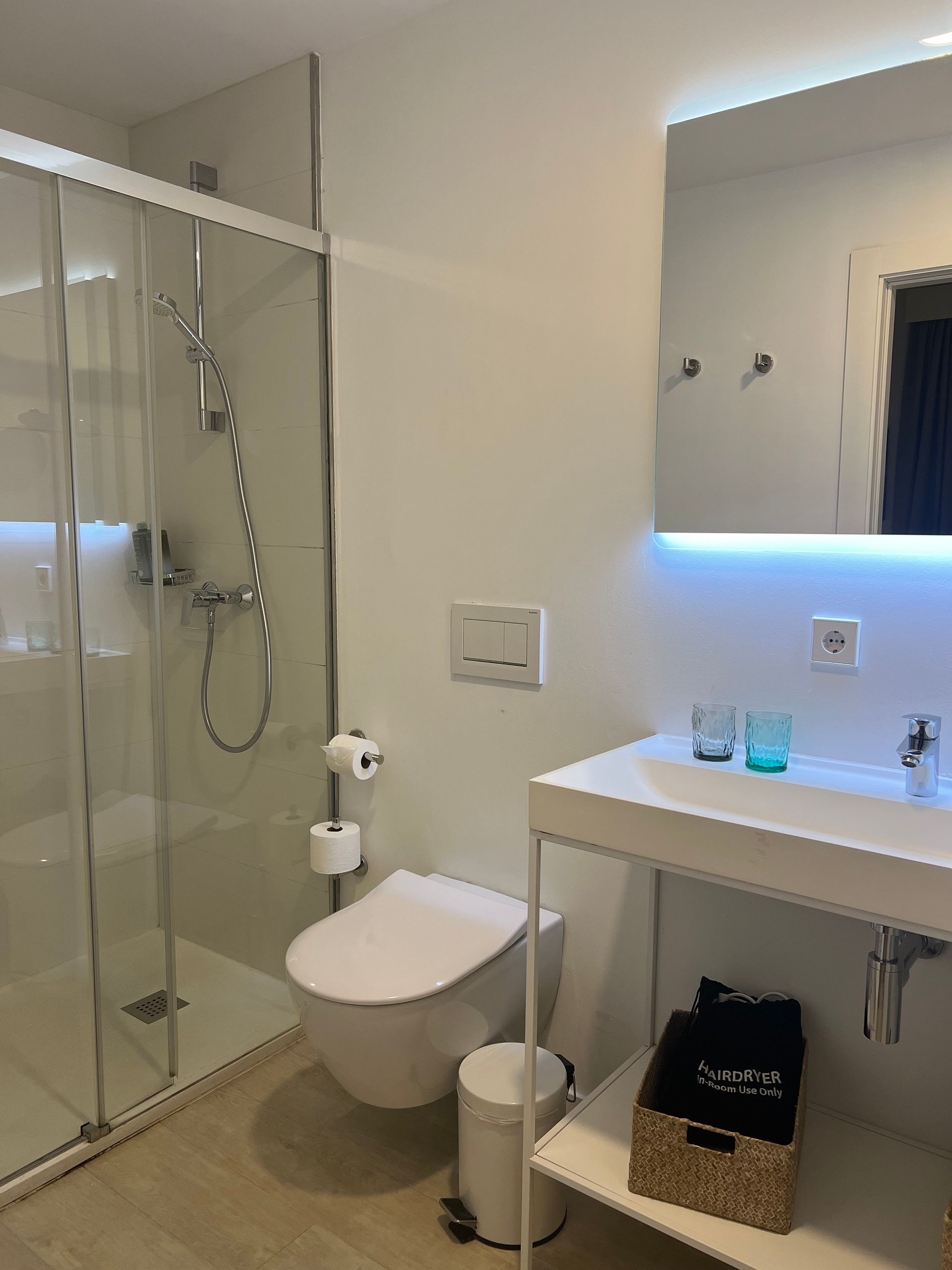 Modern bathroom with shower, toilet, sink, and mirror. Soft white and chrome finishes.