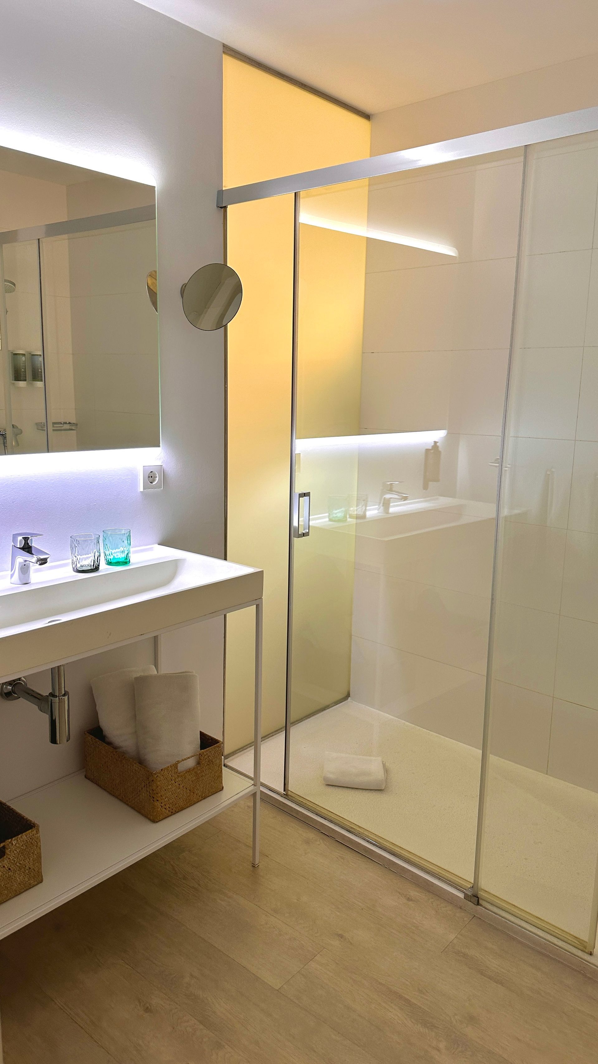 Modern bathroom with a glass shower, white vanity, and light wood flooring.