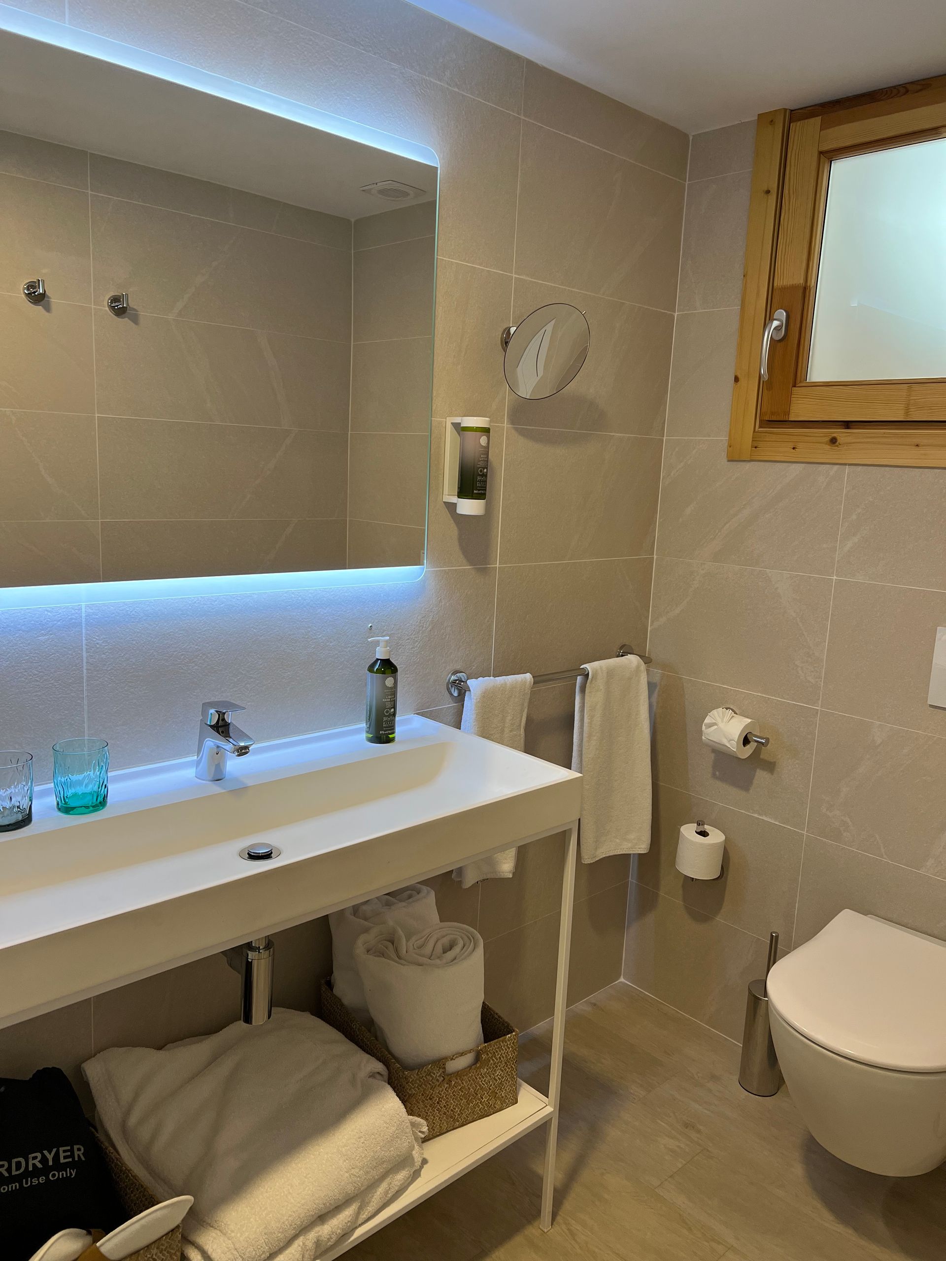 Bathroom with white sink, toilet, beige walls, and wooden window frame.