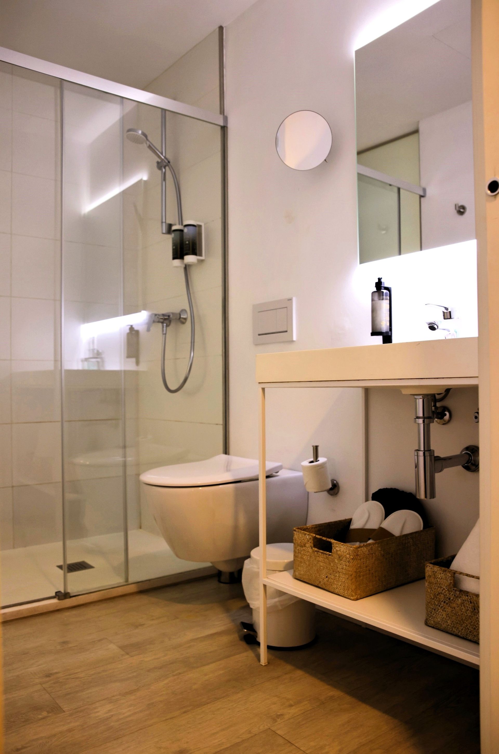 Modern white bathroom with a walk-in shower, toilet, open vanity with storage, and wood-look flooring.