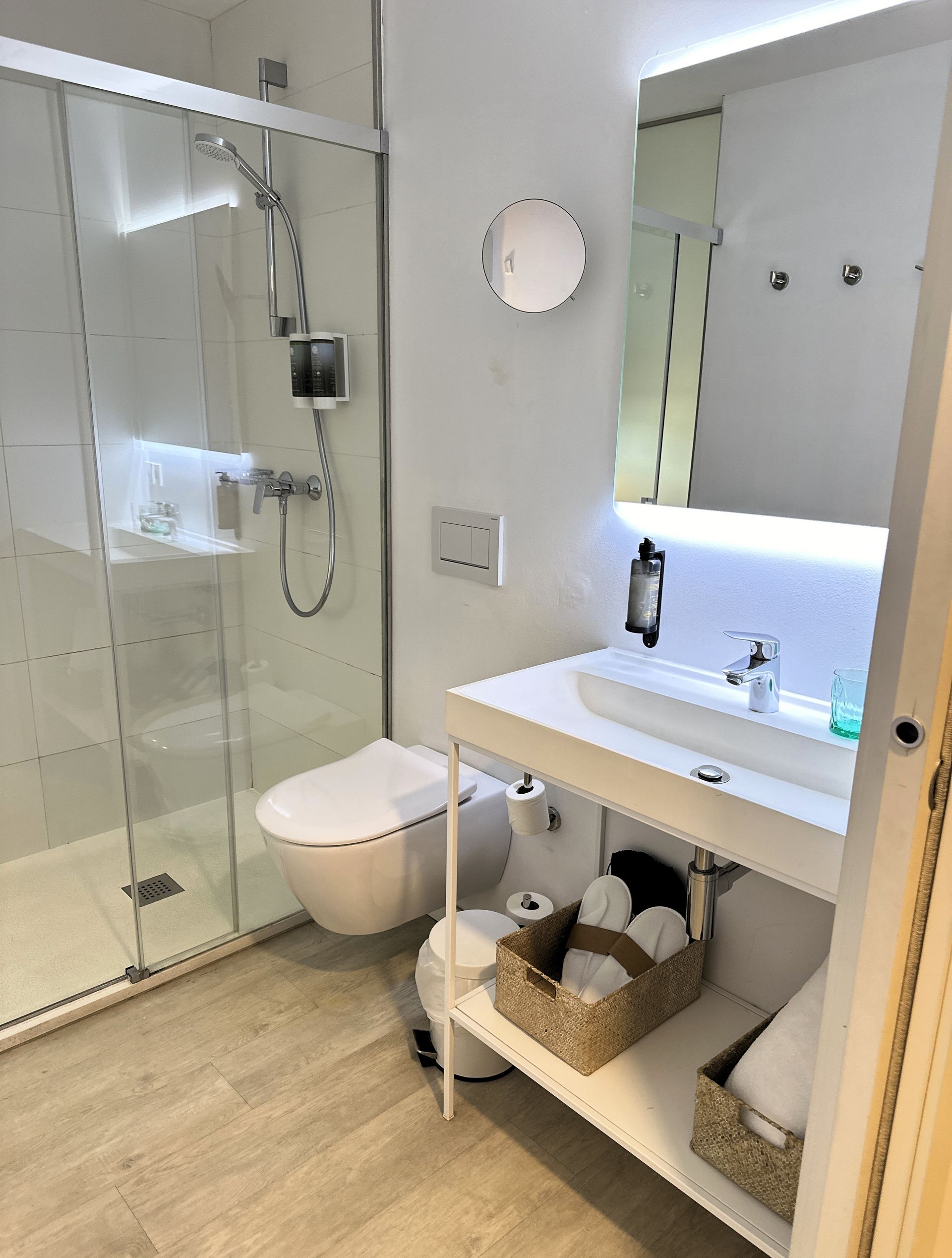 Bright, modern bathroom with glass shower, white fixtures, and light wood-look floor.