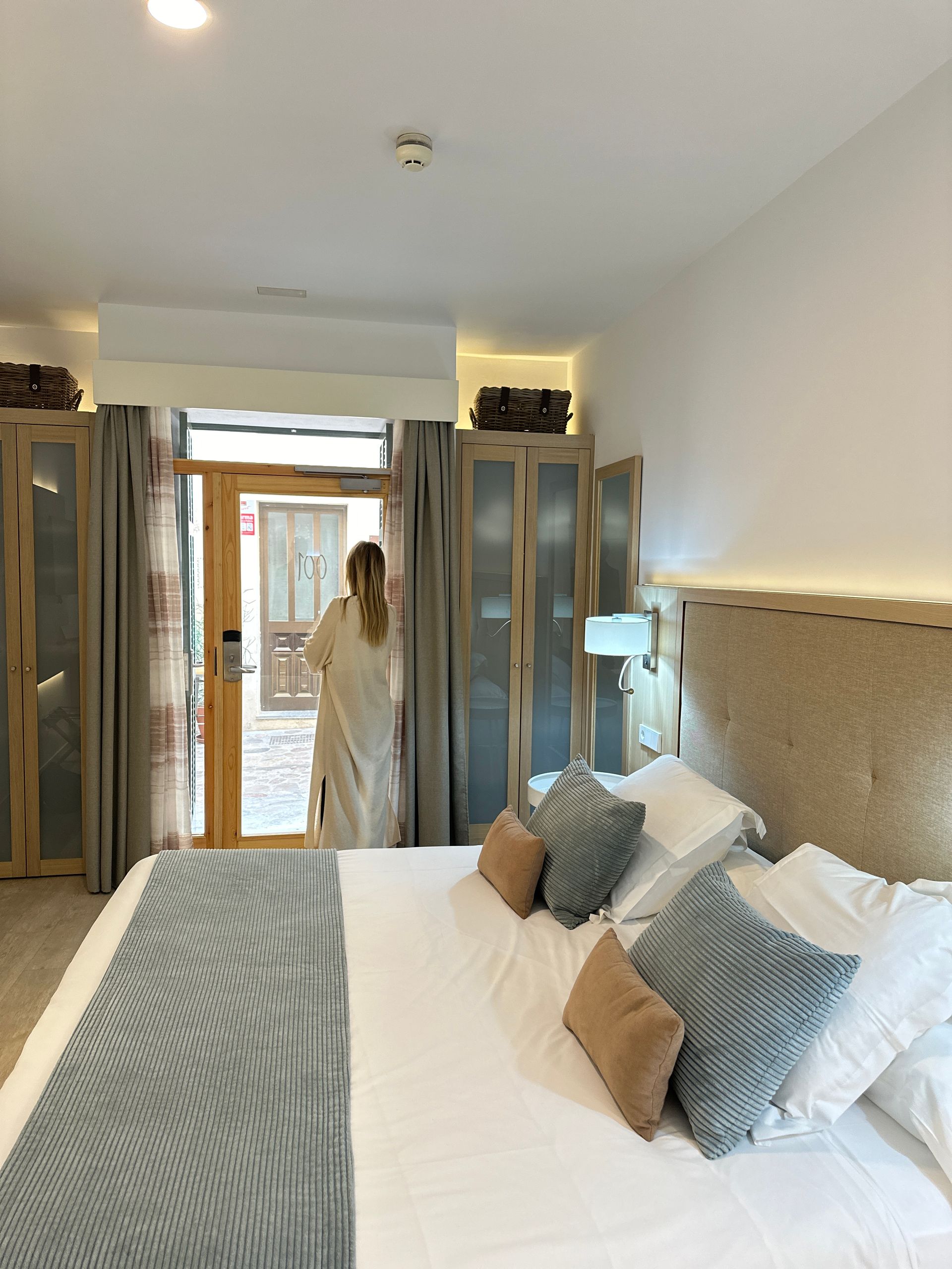 Woman in robe entering bedroom with large bed, door to outside, light decor.