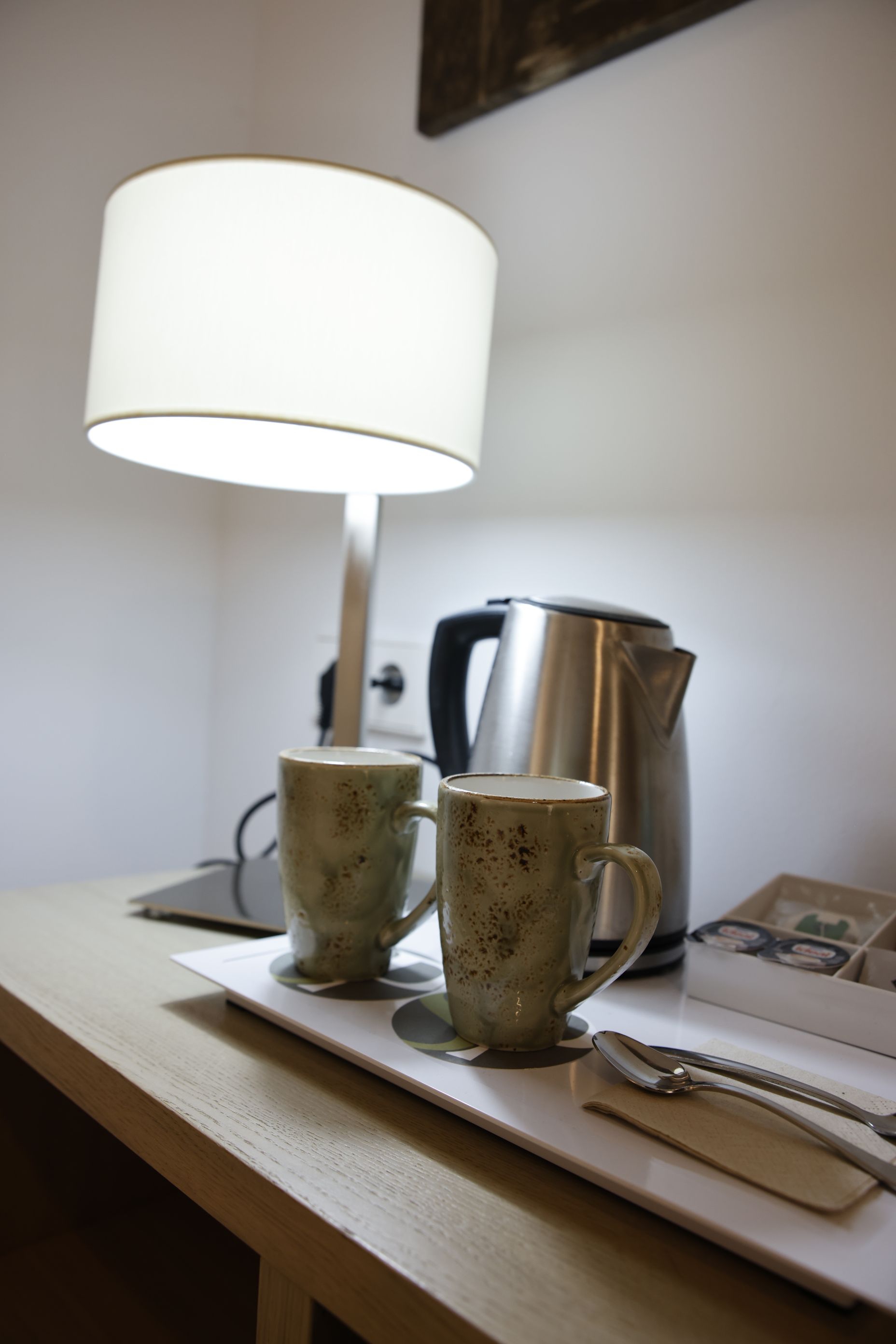 Two mugs, electric kettle, and lamp on a wooden table.