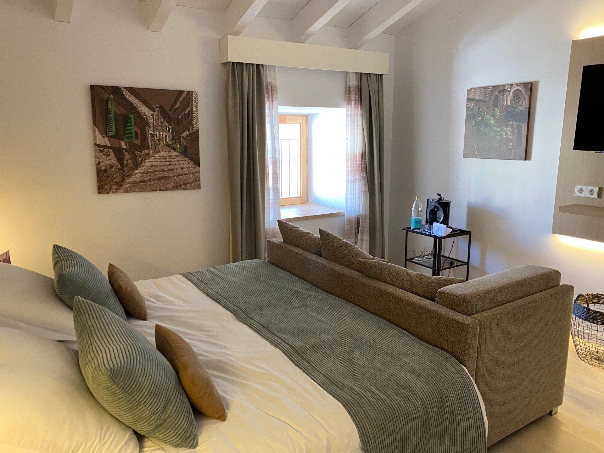Dormitorio con cama y sofá. Obras de arte en las paredes y una ventana con cortinas.