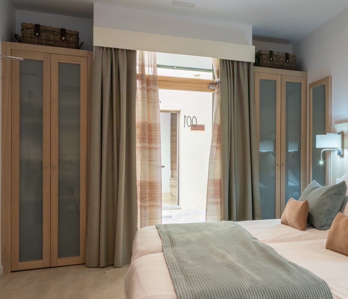 Chambre avec un lit, deux armoires et une porte menant à un couloir, palette de couleurs neutres.