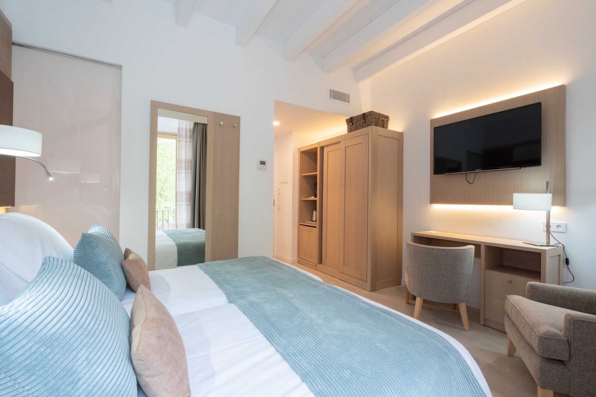 Bedroom with light wood furniture, bed with blue and pink accents, TV, and mirror.