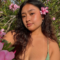 Young person of color with dark brown hair and a pink flower in it. 
