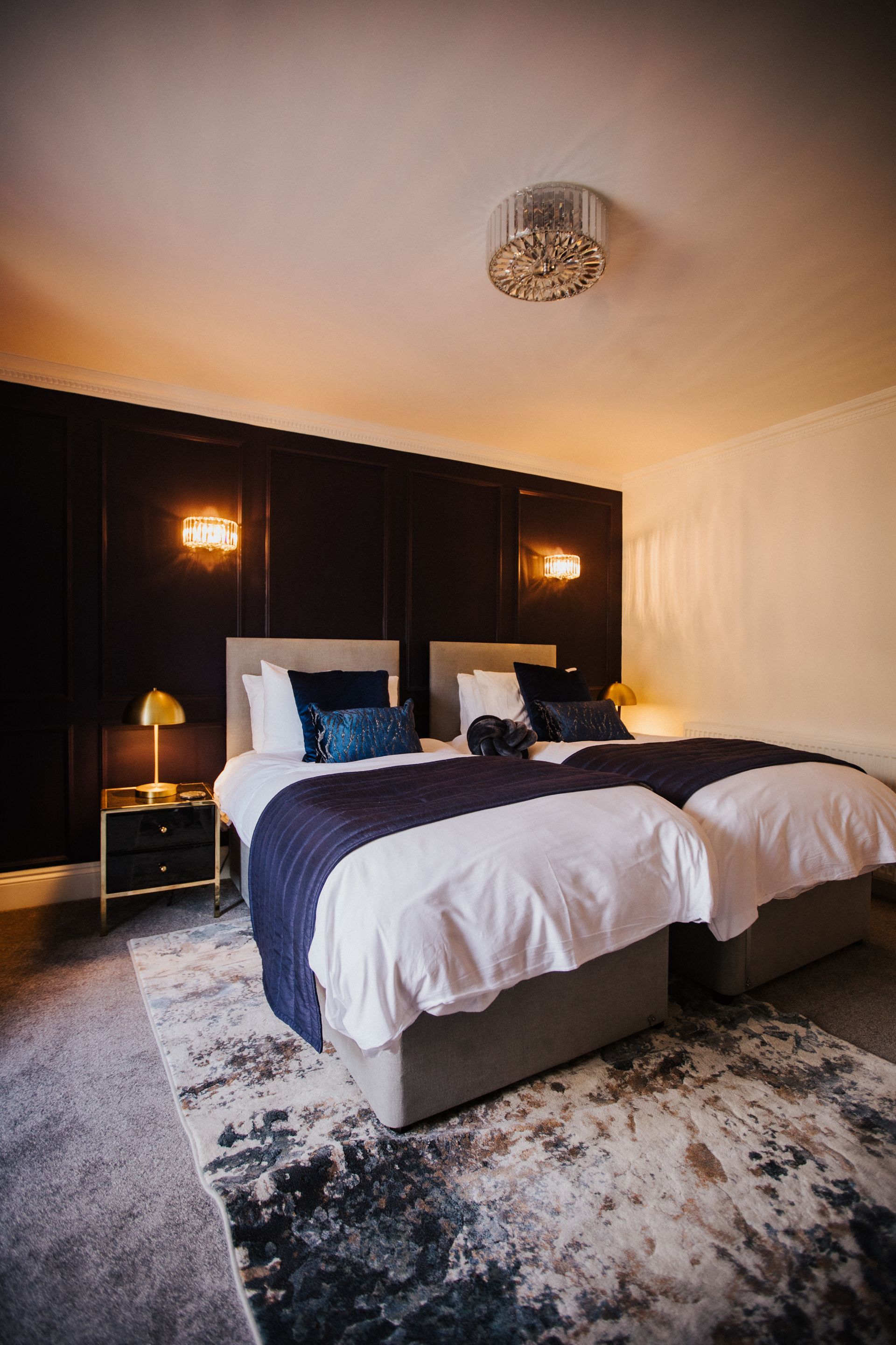 Bedroom with a bed, desk, and accent wall with sconces, in neutral colors.