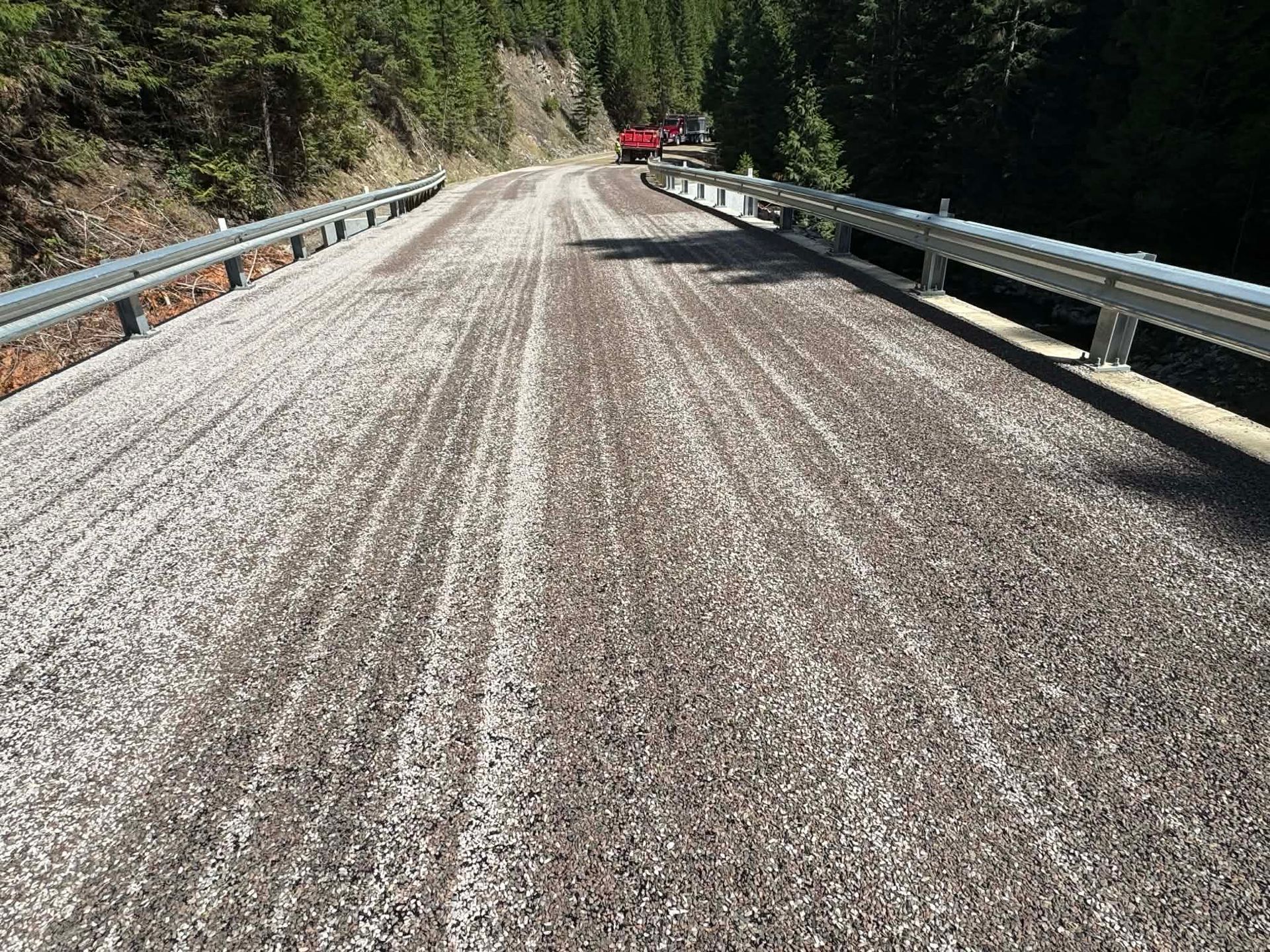 Fresh chip seal road paving project on a mountain roadway with protective guardrails in Great Falls, Montana