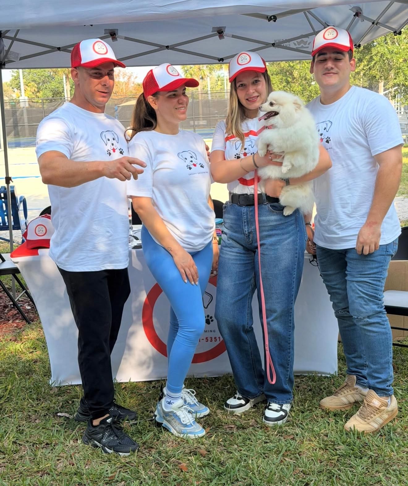 The Snoopy Grooming team in uniform holding a white dog