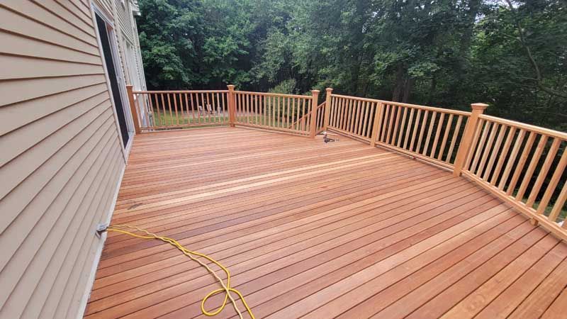 A large wooden deck with a wooden railing is in front of a house.