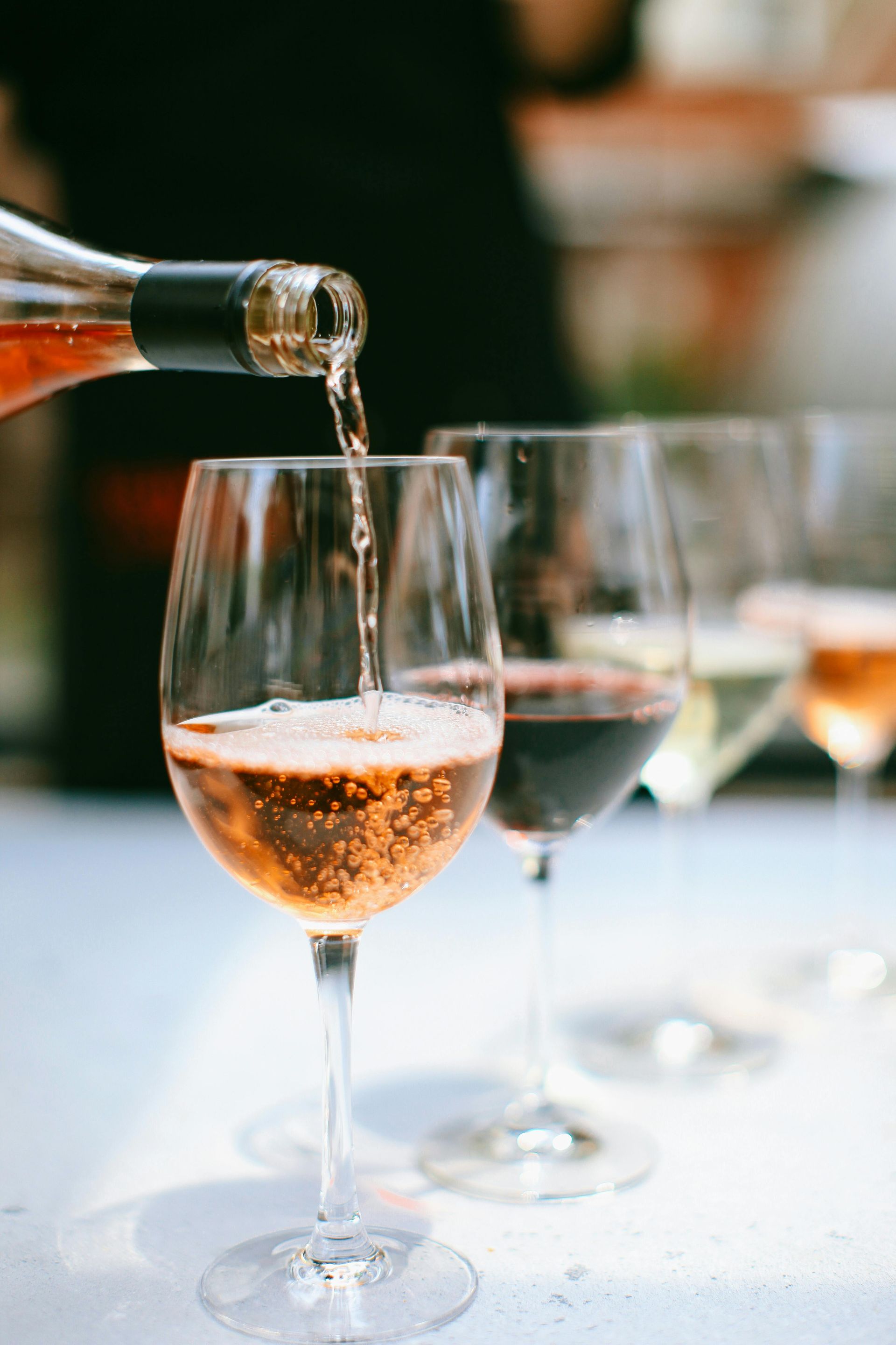 Vino rosado maxia vertido en una copa con tallo, con otras copas de vino en el fondo.