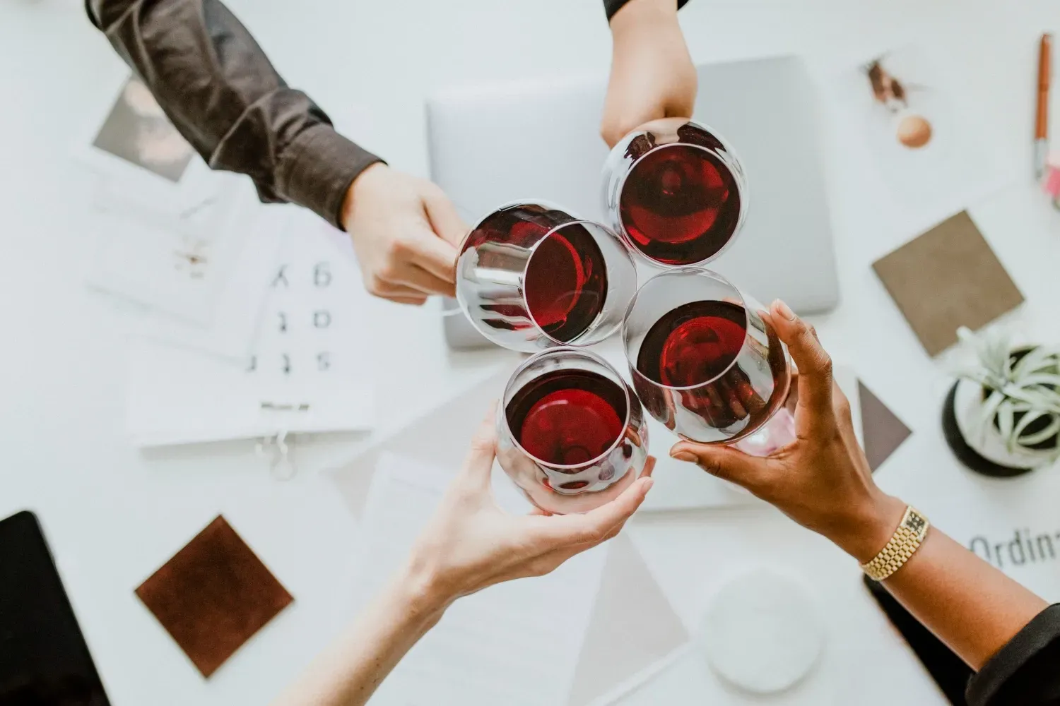 Cuatro personas brindando con copas de vino tinto maxia alrededor de una mesa blanca.