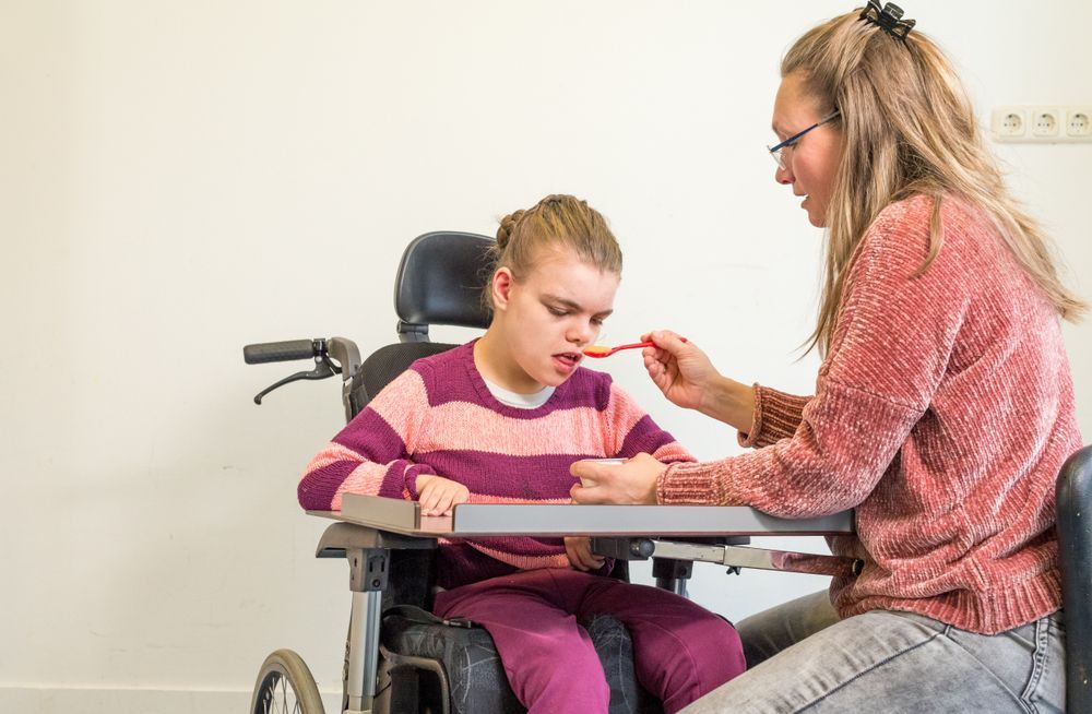 Caregiver Feeds a Child Seated in a Wheelchair at a Table — XL Care in Ayr, QLD