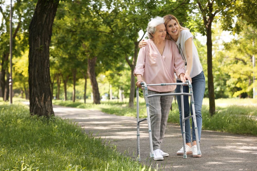 Two Women Walking With a Walker on a Tree-lined Park Path — XL Care in Ingham, QLD