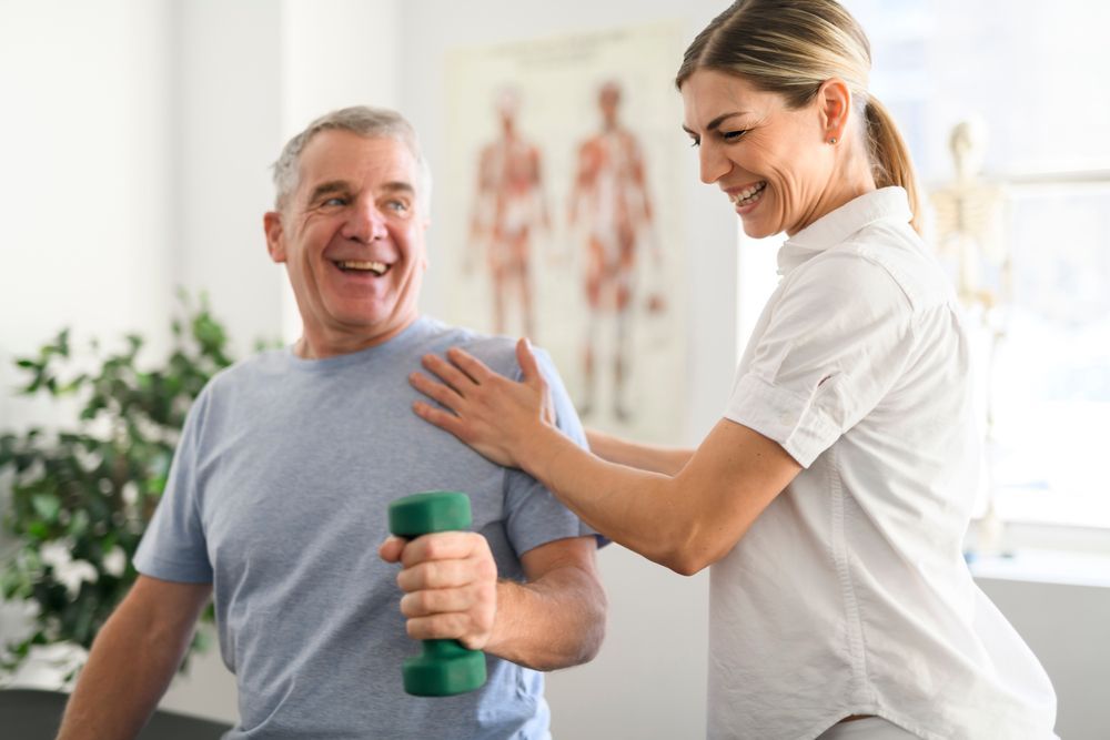 Physical therapist assisting a smiling patient holding a green dumbbell — XL Care in Ayr, QLD