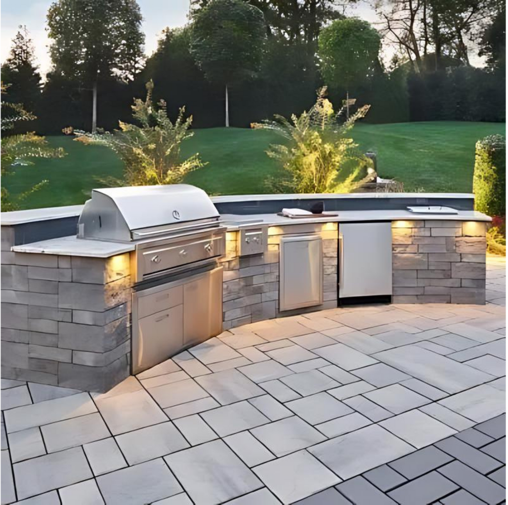 Outdoor kitchen with stainless steel grill, refrigerator, and countertop, built into a stone structure.