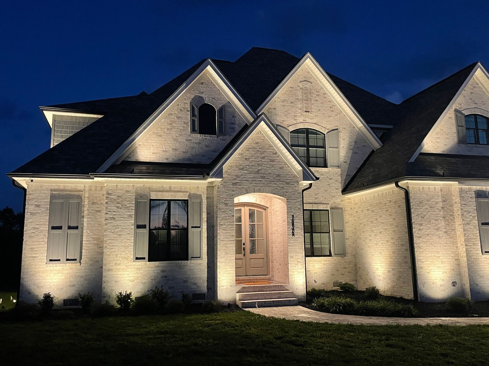 Illuminated white brick home at night with lights outlining the roofline and highlighting the facade.