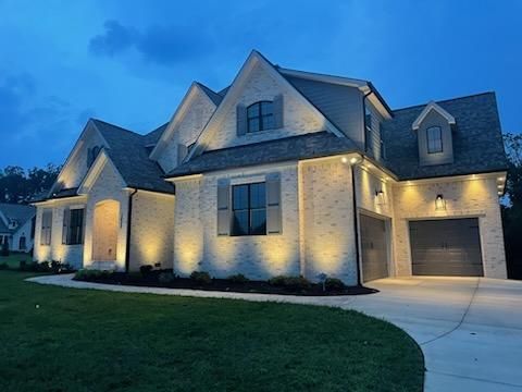 Two-story brick house illuminated at night with a paved driveway and green lawn.
