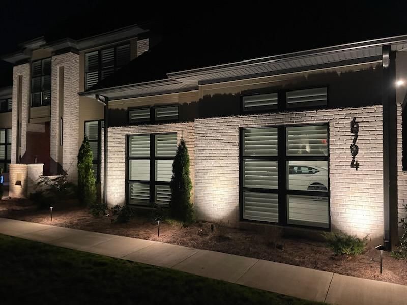 Exterior of a modern building illuminated by spotlights at night. Brick and windows with landscaping.