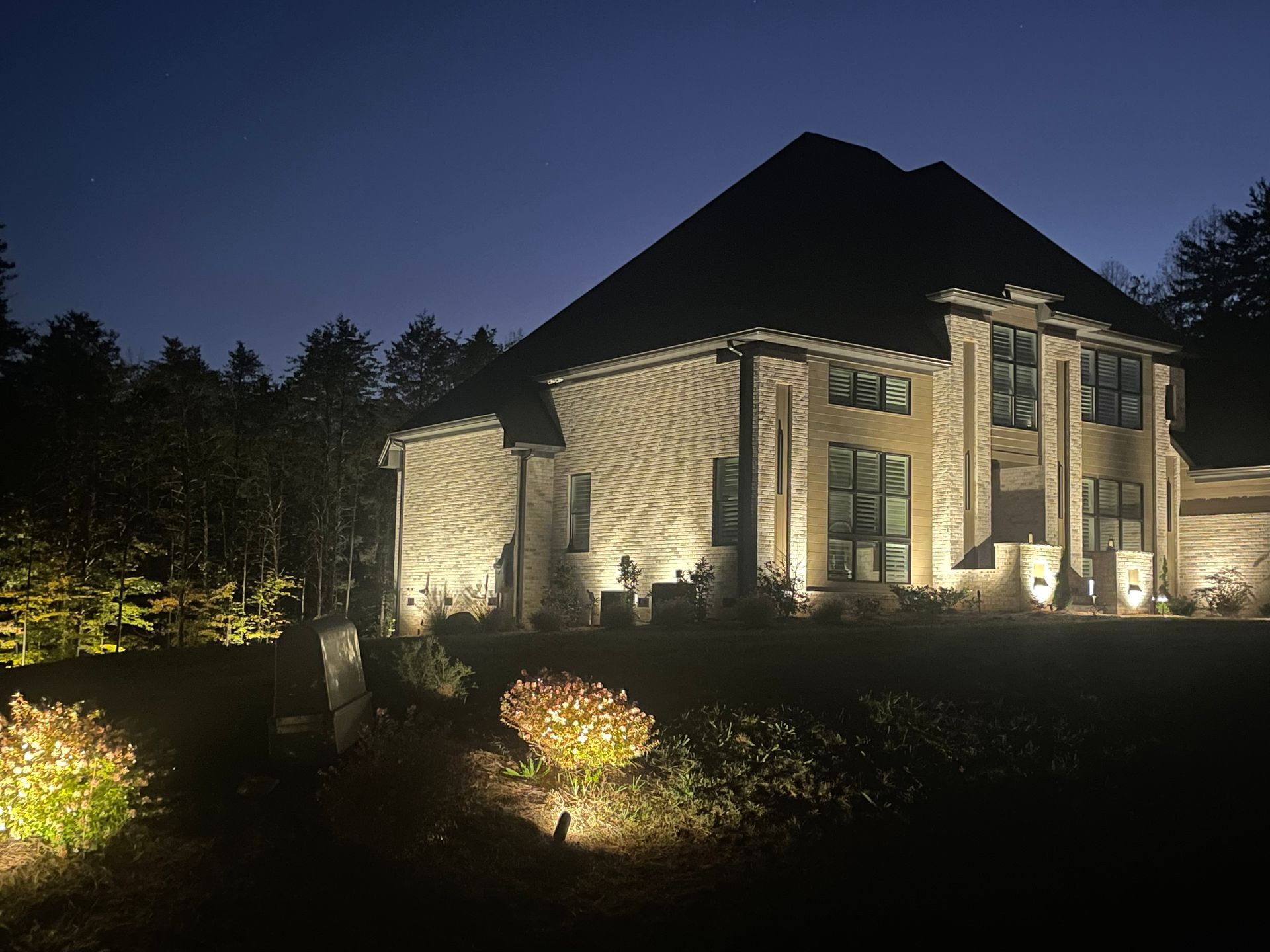 Large brick house illuminated at night by landscape lighting.