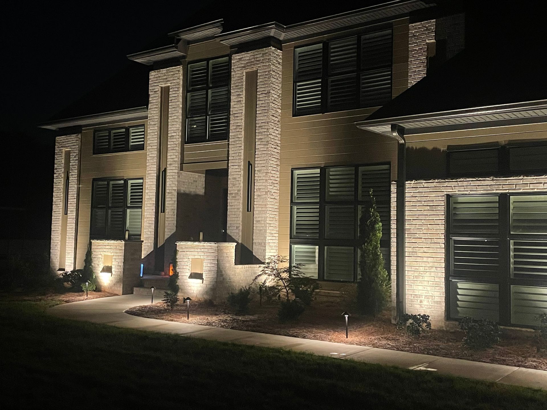 Lit-up modern home at night with pathway lights illuminating the facade.