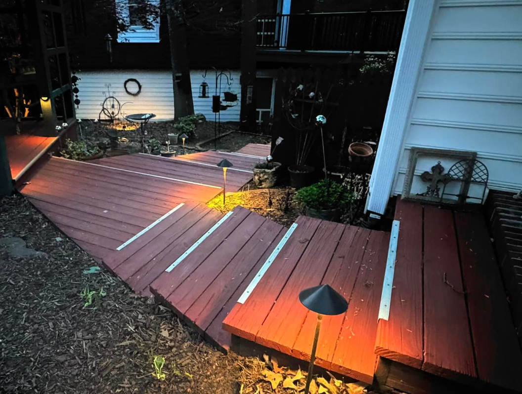 Red deck with white stripe lighting leading to a yard, lit at dusk.