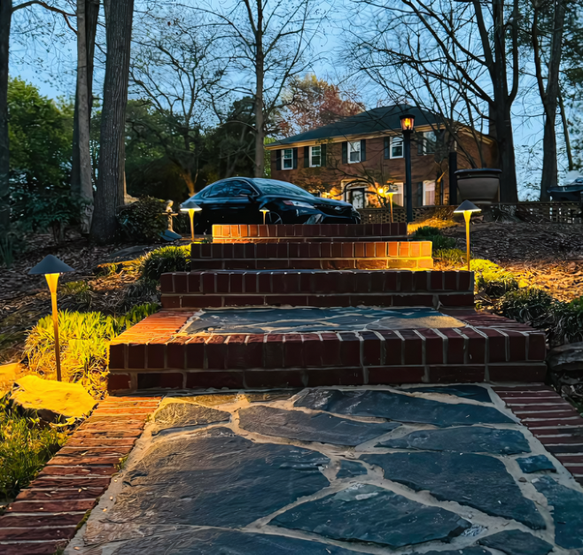 Brick stairs with pathway lights leading to a house, with a car parked nearby. Dusk setting.