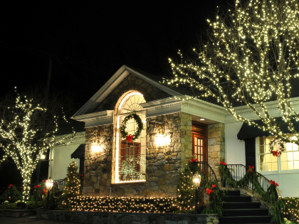 House decorated with white Christmas lights, illuminated at night. A stone facade with a wreath and garland.